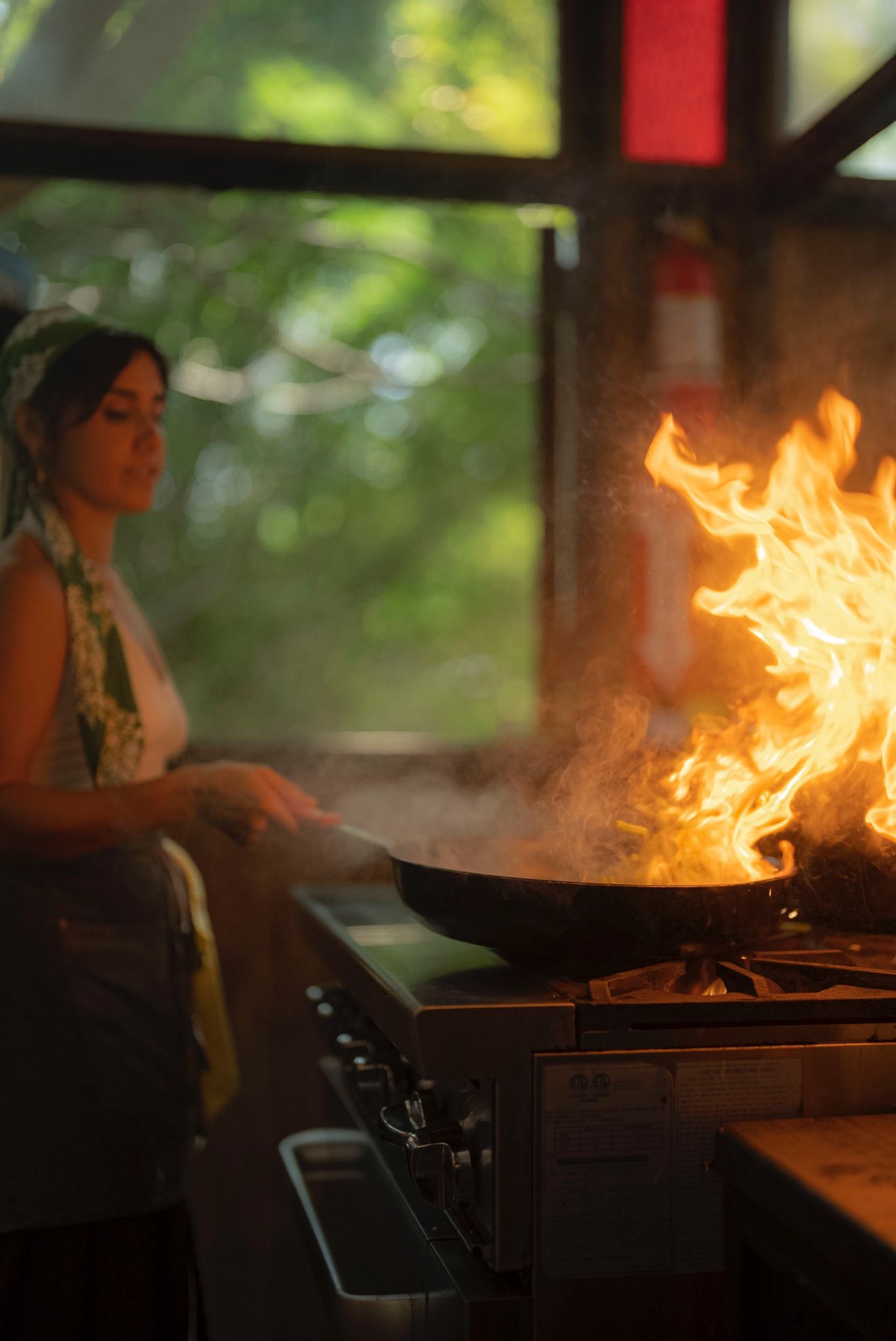 Cocinera salteando en un sartén en llamas en una cocina abierta