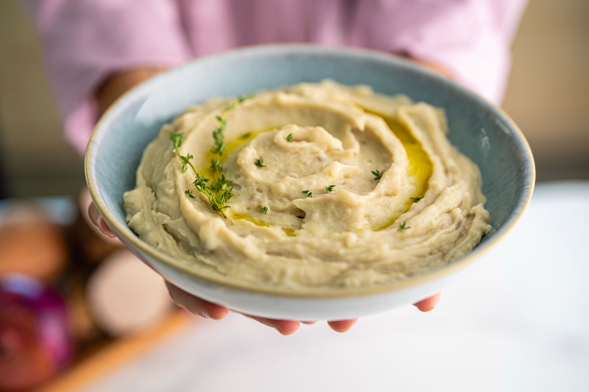 Manos sosteniendo un plato de hummus con aceite de oliva