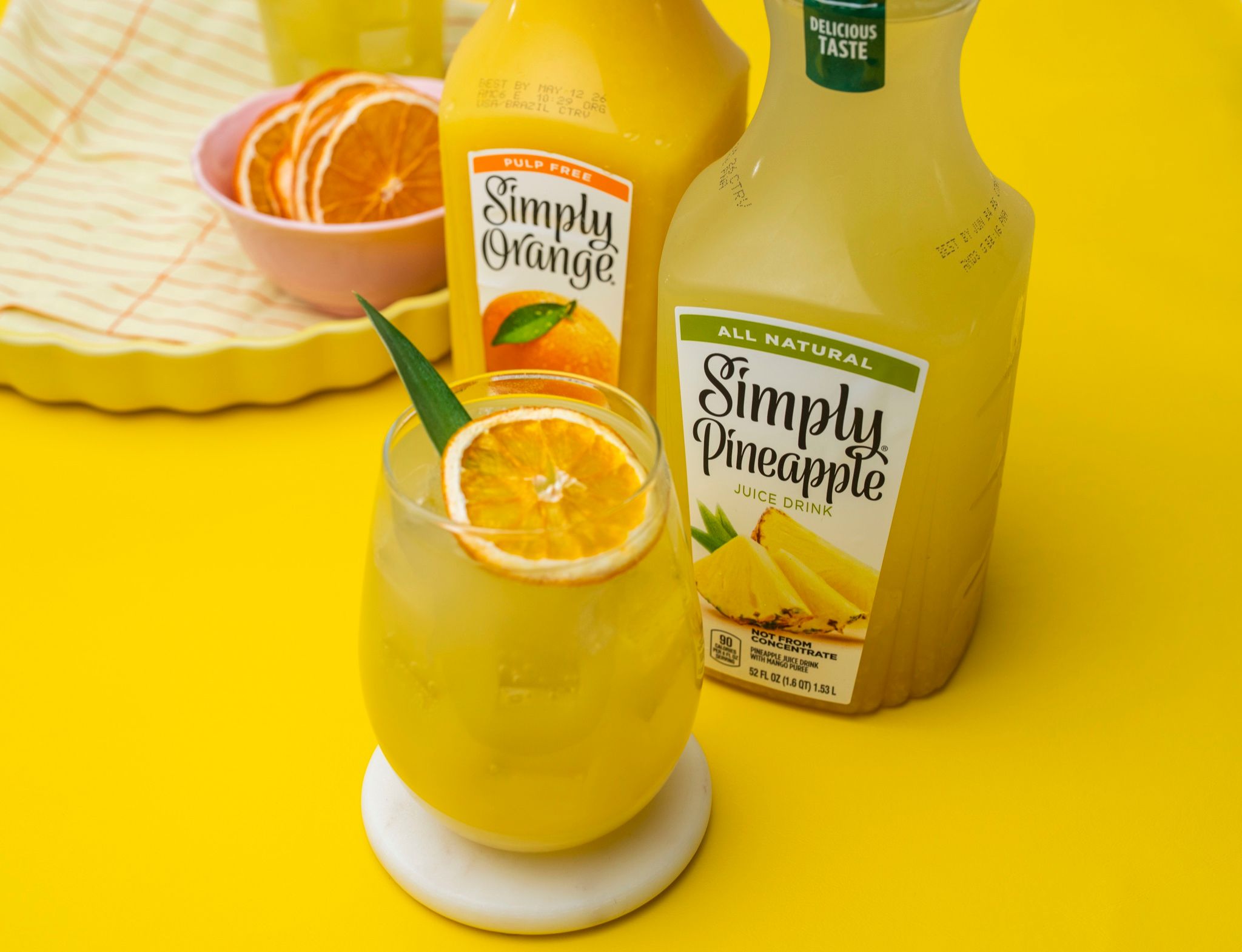 Botella de jugo de piña y vaso sobre fondo amarillo
